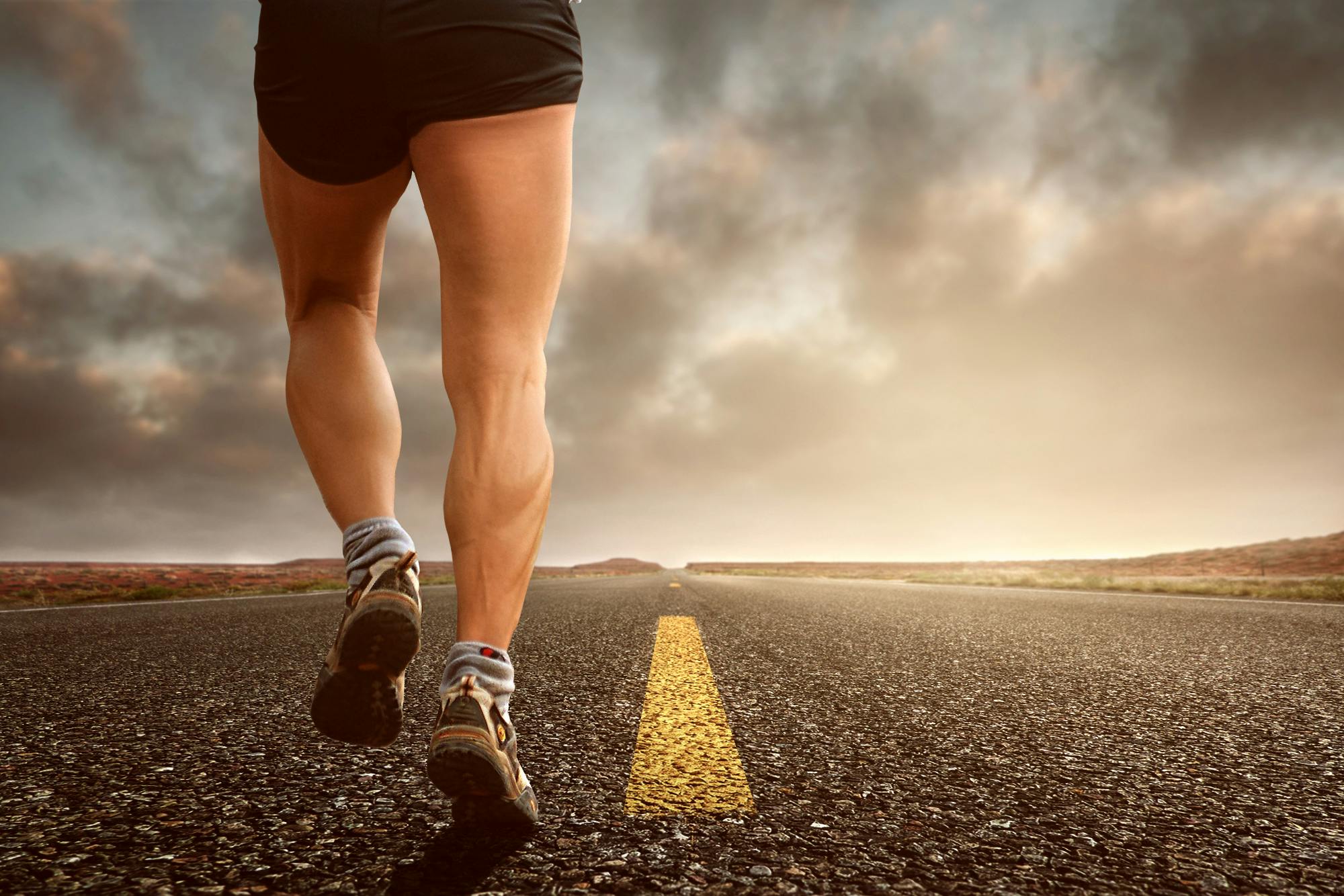 Runner's legs on a road during a sunset, symbolizing endurance and outdoor fitness training.